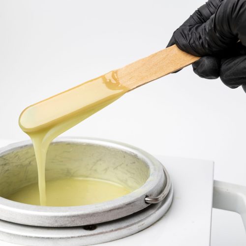 Human hand holding wooden sticks with wax over wax melter A human hand holding wooden sticks with wax over wax melter