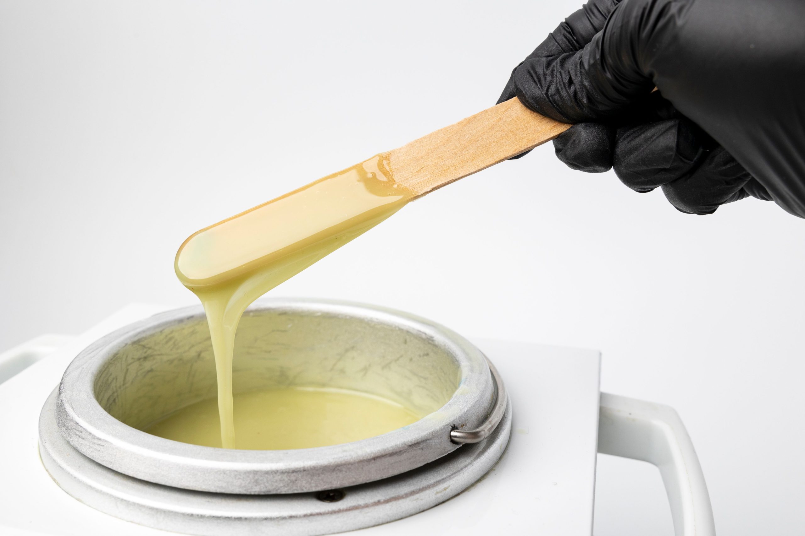 Human hand holding wooden sticks with wax over wax melter A human hand holding wooden sticks with wax over wax melter